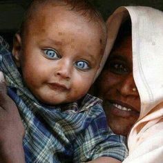 a woman holding a baby with blue eyes and a blanket over her head, smiling at the camera