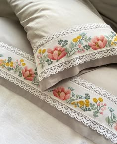 two decorative pillows on a bed with white linens and lace trim around the edges