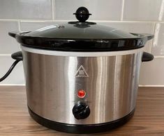 a stainless steel slow cooker sitting on top of a wooden table next to a white tile wall