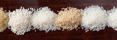 five different types of rice laid out on a wooden surface, all in the same row