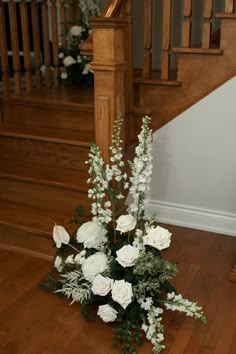 a bouquet of white flowers sitting on top of a wooden floor next to a stair case