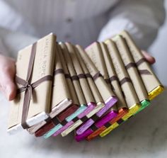 a person is holding a stack of small boxes with different colored ribbons on them and wrapped in brown paper