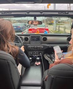 two women sitting in the driver's seat of a car, looking at their cell phones