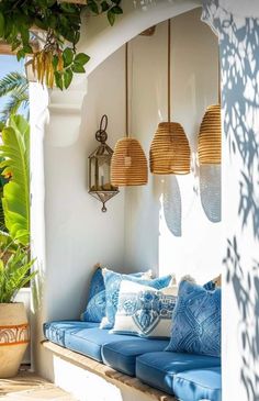 an outdoor seating area with blue cushions and hanging lights on the wall, next to potted plants