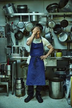 a man in an apron is holding his head while standing in front of pots and pans