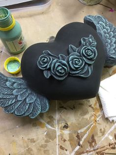 a heart shaped rock with wings and roses on it, surrounded by other crafting supplies