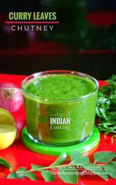 curry leaves chutney in a glass bowl on a red tray next to garlic, lemon and cilantro