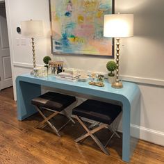 a blue console table with two stools and a painting on the wall behind it