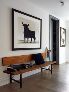 a wooden bench sitting in front of a painting on the wall next to a book shelf