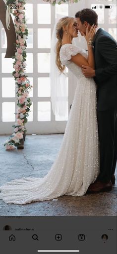 a bride and groom kissing in front of an arch with pink flowers on the side