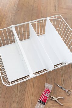 a white wire basket with scissors and other items on the floor next to it,