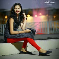 a woman in red pants and black top is sitting on a cement wall with her legs crossed