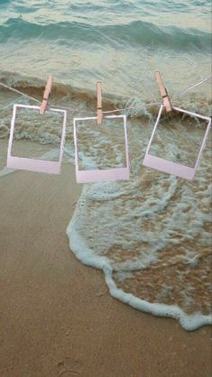 three square frames hanging from clothes pins in the sand at the ocean's edge