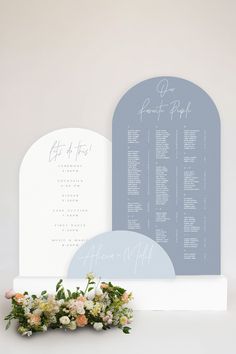 a wedding seating chart and flowers on a white table with a blue arch in the background