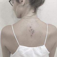 a woman with a flower tattoo on her upper back neck and behind her is a white tank top