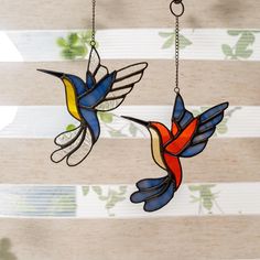 two stained glass hummingbirds hanging from chains on a striped wallpapered window curtain