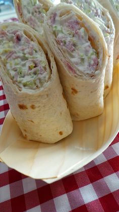 three burritos on a plate with a red and white checkered tablecloth