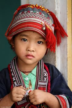 a little boy wearing a colorful hat and holding something in his hand while standing next to a door