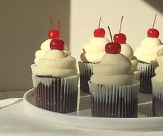 several cupcakes with white frosting and cherries on top sit on a plate