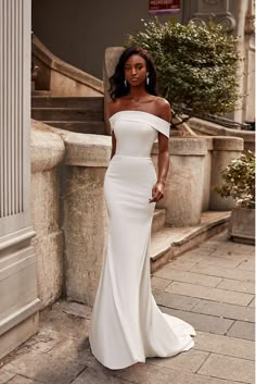 a woman in a white dress standing on the steps wearing an off - shoulder gown