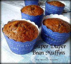 four muffins in blue paper cups sitting on a tablecloth with the words, super duper bran muffins