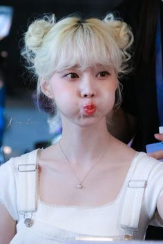 a young woman with blonde hair blowing bubbles on her nose and wearing a white dress