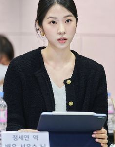 a woman sitting at a table with a tablet in front of her and another person standing behind her