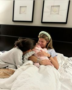 two women are laying in bed and hugging each other while the woman is holding a baby