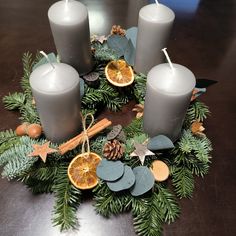 some candles are sitting on a table with pine cones and orange slices around them, surrounded by greenery