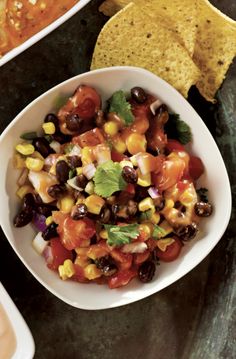 a white bowl filled with black beans, corn and tortilla chips on top of a table