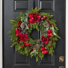 a christmas wreath with red flowers and pine cones on a black door frame, surrounded by greenery