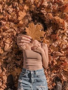 a woman laying on the ground with a leaf in front of her face, surrounded by leaves