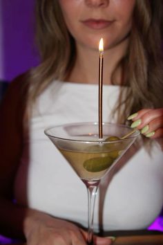 a woman holding a martini glass with olives in it and a lit candle on top