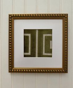 a gold frame hanging on the wall above a green and white striped wallpaper with a square pattern