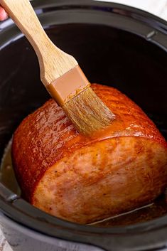 a person holding a brush in a slow cooker filled with meat