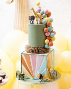 a cake decorated with animals and balloons on top of a white table next to other desserts