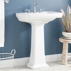 a white pedestal sink in a bathroom with blue walls and rugs on the floor