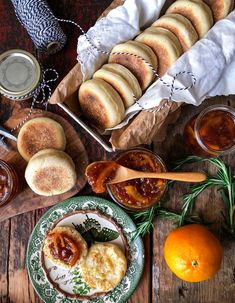 an assortment of breads and condiments on a wooden table with oranges