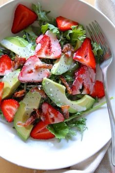 a salad with strawberries and avocado in a white bowl on a table