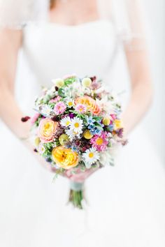 a bride holding a colorful bouquet of flowers in her left hand and looking at the camera