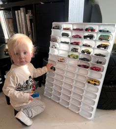 a toddler is playing with toy cars on a wall mounted display rack in front of a bookshelf