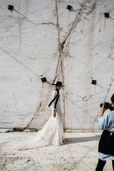 a woman in a white dress and black hat is taking a photo with her cell phone