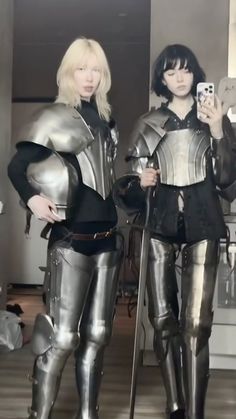 two women dressed in armor are holding cell phones and posing for the camera while standing next to each other