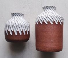 two brown and white vases sitting next to each other on top of a wall