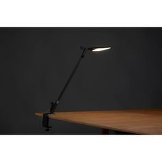 a desk lamp that is sitting on top of a wooden table in front of a dark wall