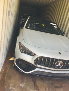 a white car is parked in a shipping container with it's hood up and headlight on