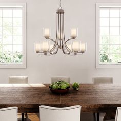 a chandelier hangs over a dining room table with white chairs and a bowl of lettuce