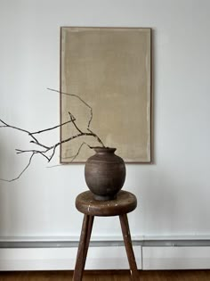 a vase sitting on top of a wooden stool next to a tree branch in front of a painting