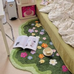 an open book sitting on top of a green rug next to a bed with white sheets