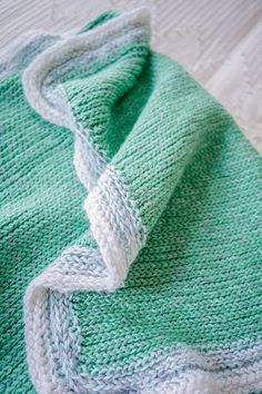 a green and white knitted blanket laying on top of a bed